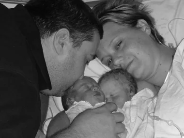 A grieving couple embraces their newborn twins, one living and one stillborn, in a tender hospital moment.