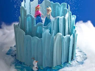 Icy cake with figures resembling Anna, Elsa, and Olaf from Frozen, surrounded by snowy decorations.