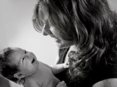 Smiling mother holding her newborn baby, both gazing lovingly at each other in a black and white photo.