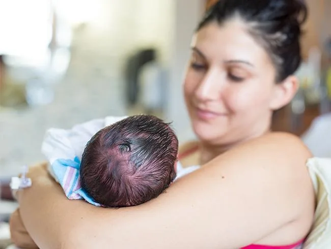 Mother holding newborn baby using a skin-to-skin C-section drape, promoting bonding immediately after birth.