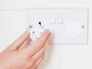 Hand placing a socket cover on an electrical outlet for child safety.