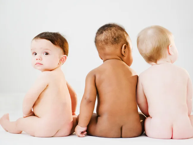 Three babies sitting on the floor, viewed from the back, with one facing slightly toward the camera.