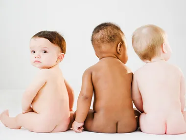 Three babies sitting on the floor, viewed from the back, with one facing slightly toward the camera.