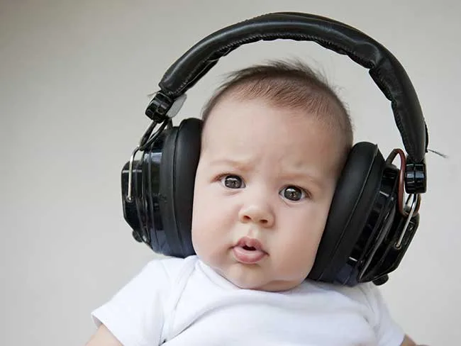 Baby wearing oversized headphones, looking curious with a slight frown.