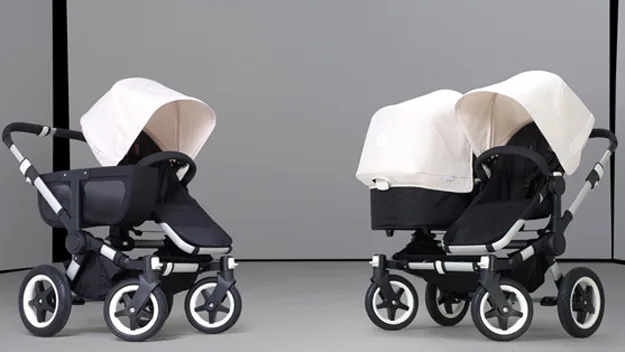 Two high-end strollers with white canopies and black seats on a grey background.