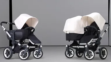 Two high-end strollers with white canopies and black seats on a grey background.