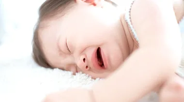 A baby lying down, crying on a soft white surface.