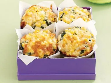Corn and spinach muffins in a purple box, lined with parchment paper.