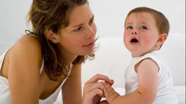 A concerned woman comforts a young child who appears to be upset, sitting together on a bed.