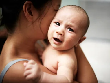 Mother holding a baby who looks upset, providing comfort and soothing in a tender moment.
