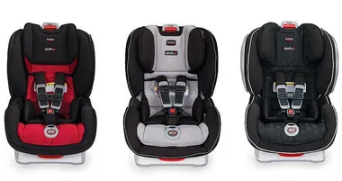 Three Britax car seats in different colors: red, grey, and black, showing front view with harnesses.