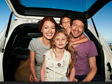 A family of four smiling in the back of an open car trunk.