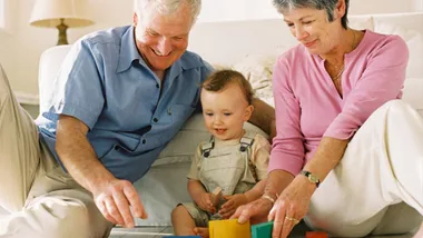 Grandparents and toddler playing with colorful blocks on the floor, smiling and engaging together.