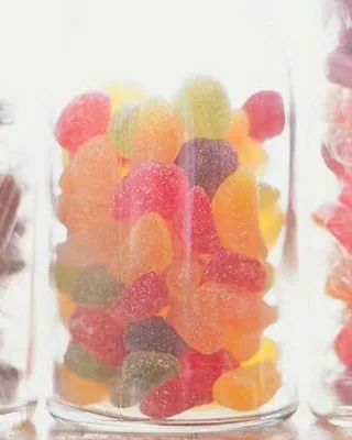 A clear jar filled with colorful sugar-coated jelly candies in various shapes and sizes.