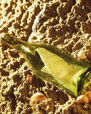 Green bottle containing a rolled paper, half-buried in sand with seashells around.