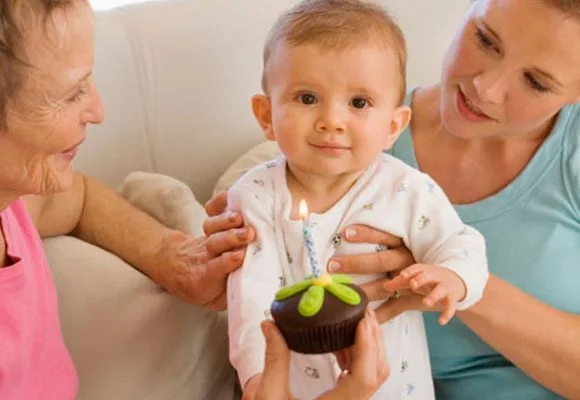 Baby holding a cupcake with a candle, with two adults smiling beside them.