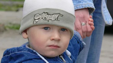 Toddler holding an adult's hand, wearing a hat labeled "Street," depicting road safety awareness.