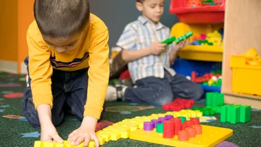 Two children playing with colorful building blocks on a carpeted floor.