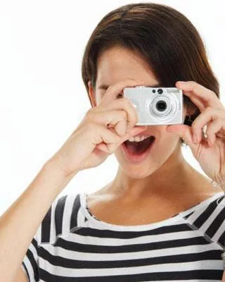A woman in a striped shirt playfully takes a photo with a compact digital camera.