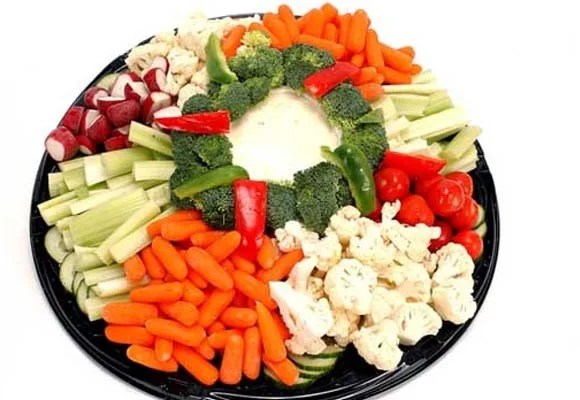 Platter of fresh vegetables including carrots, broccoli, cauliflower, and radishes arranged around a dip.
