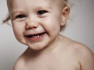 Smiling baby with visible teeth, close-up shot.