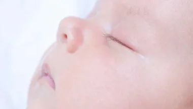 Close-up of a peacefully sleeping baby's face, showing soft skin and closed eyes against a light background.