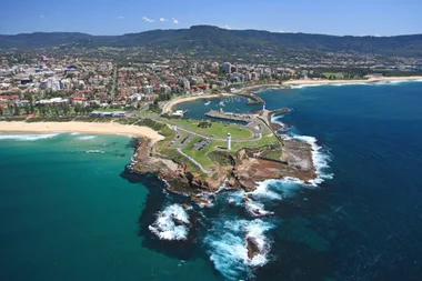 Aerial view of Wollongong, featuring coastline, beaches, a lighthouse, and cityscape with greenery and mountains in the background.
