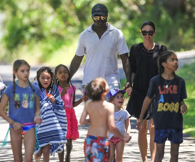 A group of people, including adults and children, walk together outdoors in a sunny area.