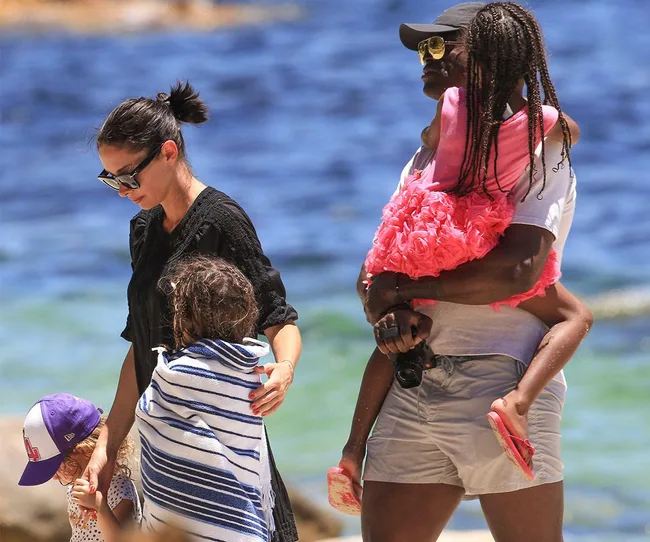 A family with children wrapped in towels enjoys a day at the beach, with the ocean in the background.