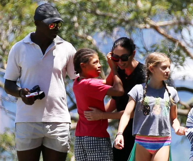 Family enjoying a sunny day outdoors, with man holding a camera and children interacting.