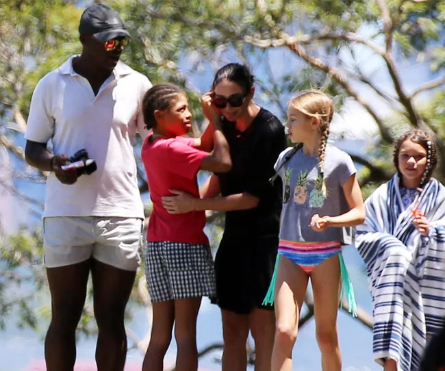 A group of five people casually dressed, two holding cameras, walking outdoors on a sunny day.