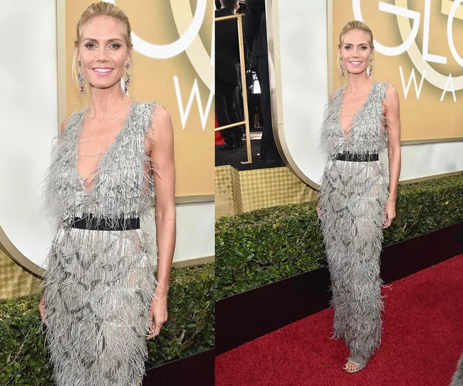 A person in a silver feathered dress poses on the red carpet at a formal event.