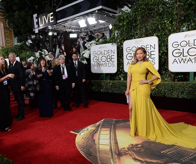 Elegant woman in a yellow gown on the red carpet at the Golden Globe Awards event, surrounded by photographers.