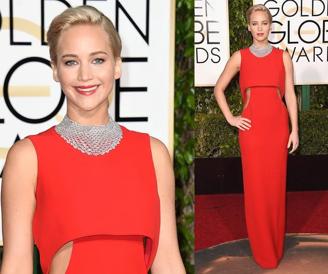 Red carpet fashion with a woman in a red gown at an awards event, standing and posing confidently.