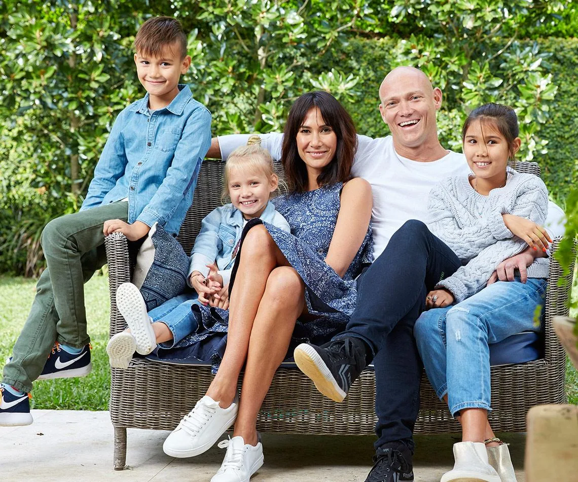 A family sitting together on an outdoor sofa, smiling, surrounded by greenery.