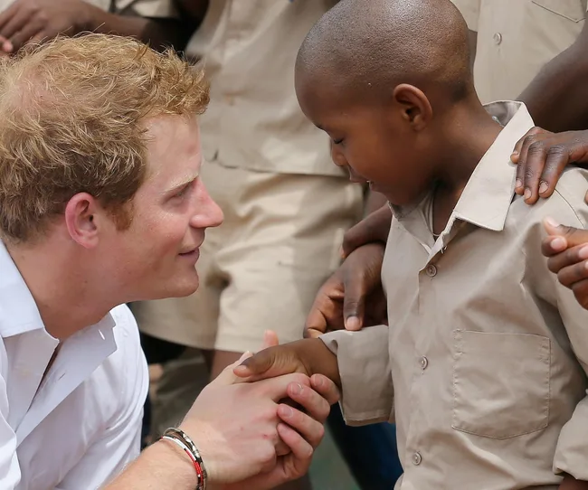 A man kneels and holds hands with a young boy in a beige shirt, surrounded by others, expressing a warm interaction.