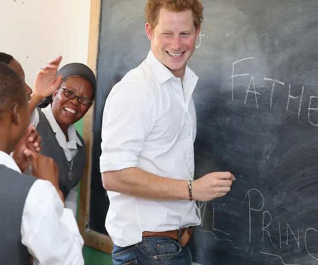 A smiling man writes on a chalkboard while a woman in a nun's habit gestures beside him.