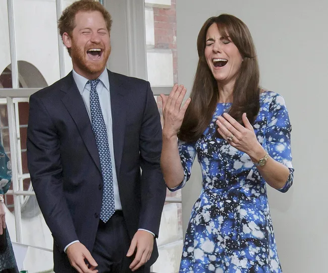 Two people in formal attire laughing and gesturing with delight indoors, near a large window.