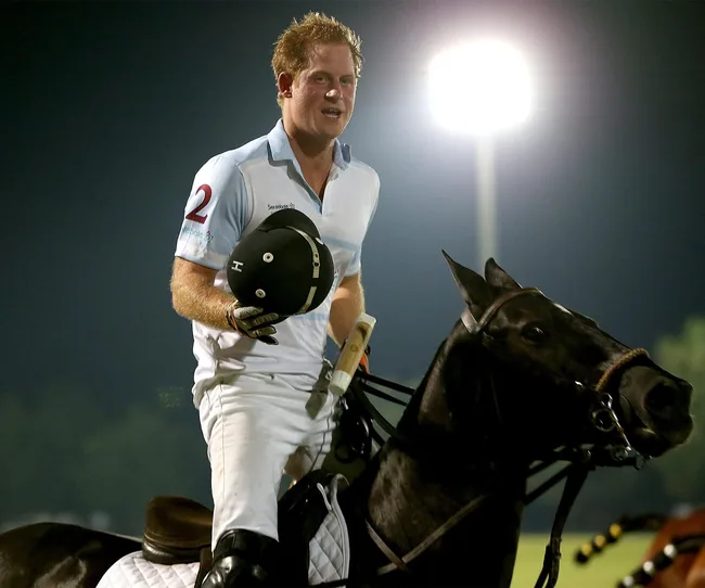 A person in a polo uniform holding a helmet while riding a horse under bright stadium lights at night.