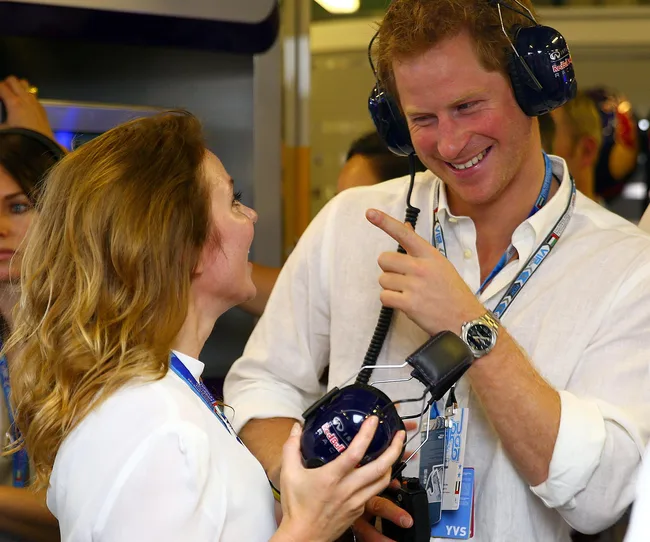 An individual wearing headphones smiles and gestures, speaking to a woman holding another pair of headphones.