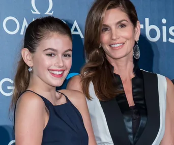 Two women smiling at a formal event, standing in front of a blue backdrop with Omega logos.