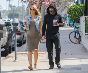 A couple walking on a sunny sidewalk, holding hands and carrying coffee cups.