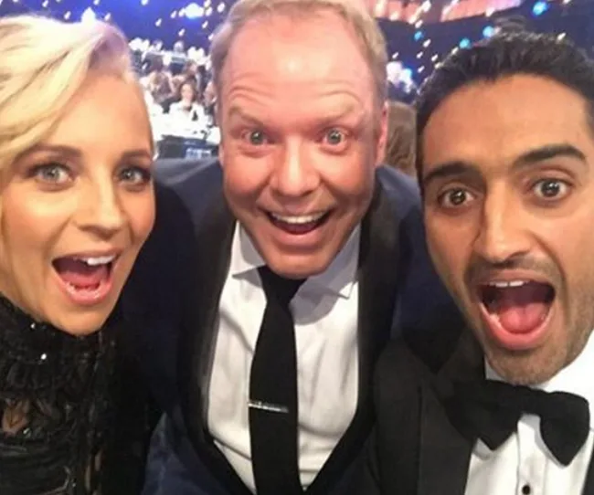 Three people taking a selfie at an event, smiling with open mouths, dressed in formal attire.