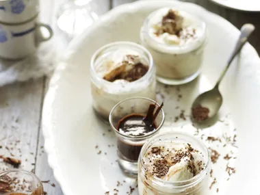 Creamy desserts in jars topped with chocolate shavings on a white plate, alongside a small glass of espresso.