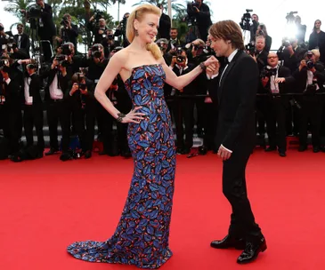 A woman in a colorful gown and a man in a suit on a red carpet, surrounded by photographers.
