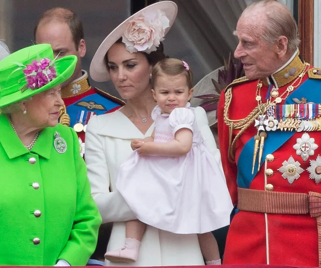 A family stands on a balcony at a formal event, with a woman in white holding a child in pink.