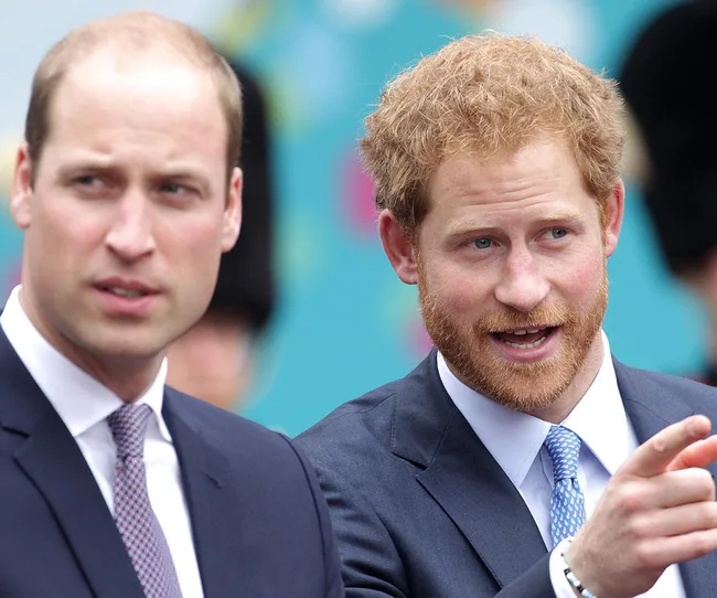 Two men in suits talking at an outdoor event; one points while the other looks on.