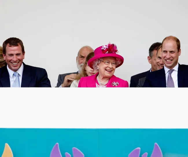 Three people smiling in an audience; one elderly woman in a bright pink outfit and hat flanked by two men in suits.