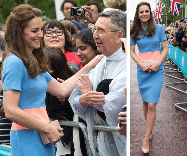 A woman in a blue and pink dress greets people at an outdoor event, with Union Jack flags visible in the background.