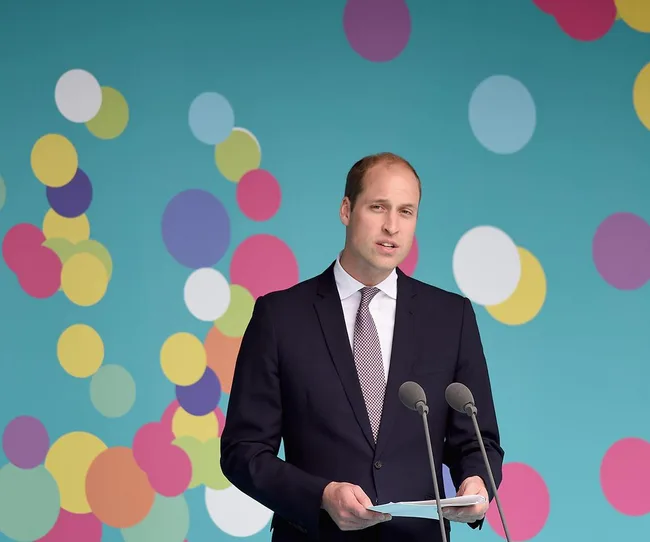 Man in a suit speaking at a podium with a colorful polka dot background.